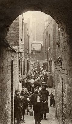 an old black and white photo of people walking down a narrow alleyway with brick walls