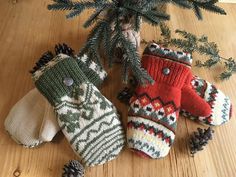 three knitted mittens sitting on top of a wooden floor next to a pine tree