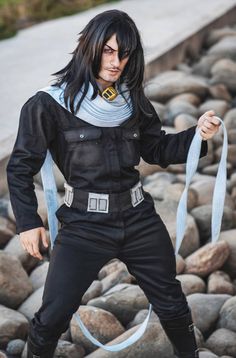 a man with long black hair holding onto a blue ribbon while standing on some rocks