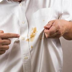 a man in white shirt holding his left hand out and pointing at the brown spot on his right chest