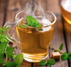 a glass cup filled with green tea next to some sugar cubes and mint leaves