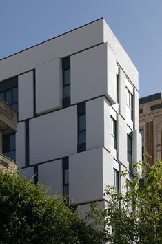 a tall white building with many windows on it's side and trees in the foreground