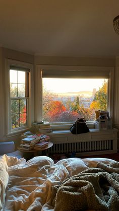 an unmade bed with blankets on it in front of two windows overlooking the city