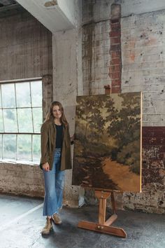 a woman standing in front of an easel with a painting on it