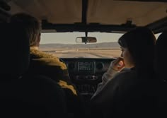 two people sitting in the back seat of a car looking out at an open field