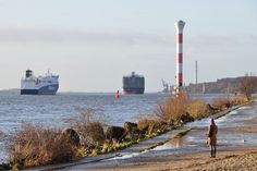 there is a man walking on the beach with two ships in the water behind him