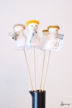 three small white angel figurines sitting on top of sticks in a black vase