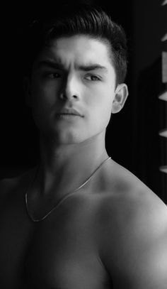 black and white photograph of a man with no shirt on, wearing a silver necklace