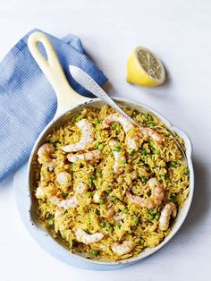 a pan filled with rice and shrimp next to a lemon wedge