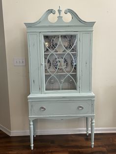 a blue china cabinet with glass doors on the top and bottom shelf, in front of a wall