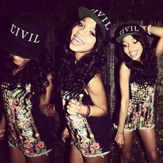 three beautiful young women standing next to each other in front of a wooden fence wearing hats