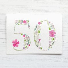 the number 50 is decorated with pink flowers and green leaves on a white wooden surface