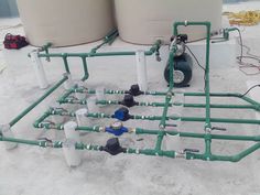 pipes and valves are lined up in the snow near tanks with water coming out of them