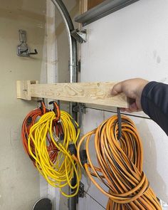 a person is holding a piece of wood with wires attached to it and there are other cords hanging on the wall