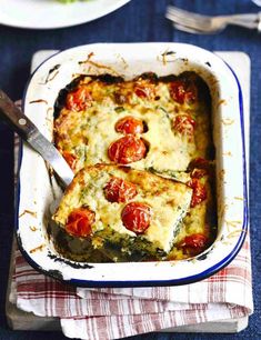 a casserole dish with tomatoes and spinach on the side next to a salad