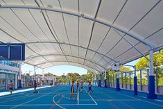 an indoor basketball court with several people playing on it and some buildings in the background