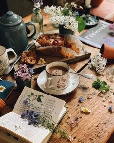 a wooden table topped with books and flowers next to a cup of hot chocolate on top of a saucer