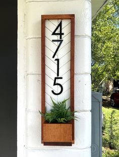 a house number sign mounted to the side of a building with a plant in it