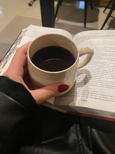 a person holding a cup of coffee and an open book