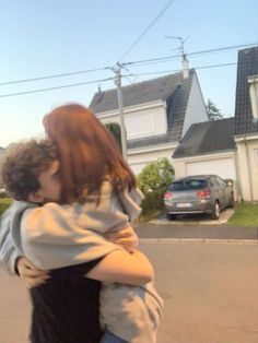 a woman is hugging a man on the street in front of a house and car