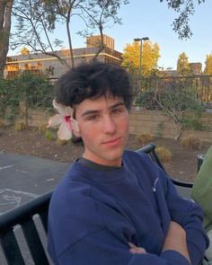 a young man sitting on top of a wooden bench next to a flower in his hair