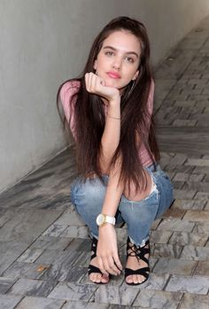 a woman sitting on the ground with her hand under her chin and looking at the camera