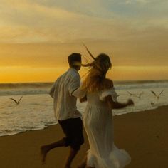 a man and woman running on the beach with birds flying in the sky behind them