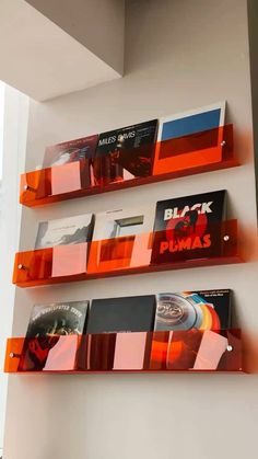 three orange shelves with cd's on them against a white wall in a room