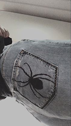 a person wearing jeans with a spider patch on the back of their pants and holding a cell phone