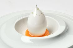 an egg sitting in a bowl on top of two white plates with orange sauce around it