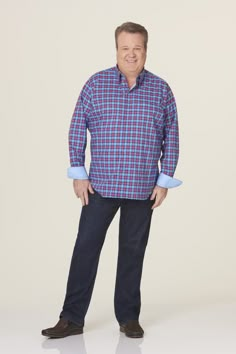 a man standing with his hands in his pockets and smiling at the camera while wearing a plaid shirt