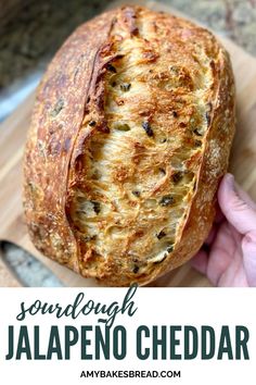 someone holding a loaf of jalapeno cheddar bread on a cutting board