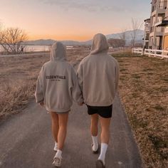 two people are walking down the road towards an apartment complex with mountains in the background