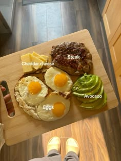 a person standing next to a cutting board with eggs, avocado and steak on it