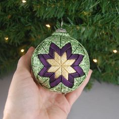 a hand holding an ornament in front of a christmas tree