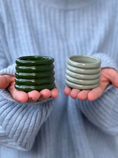 a person holding two cups in their hands, one with green tea leaves on it