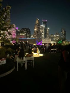 people are sitting in chairs on the grass at night with city lights in the background