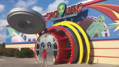 a person standing in front of a fake alien's ride at the entrance to an amusement park