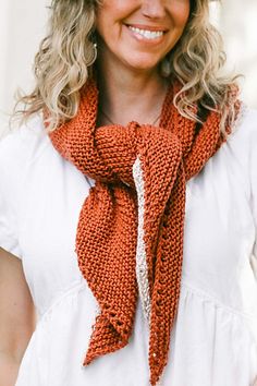 a woman wearing an orange knitted scarf and white shirt with her hands in her pockets