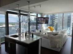 a living room filled with furniture and a large window covered in glass walls next to a kitchen