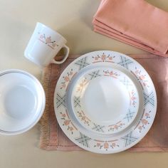 a table set with dishes, cups and napkins on top of a pink place mat