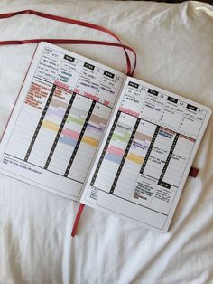 an open planner sitting on top of a bed next to a red bag and white sheets