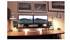 two computer monitors sitting on top of a desk next to a lamp and pictures above them