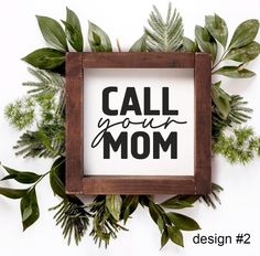 a wooden frame with the words call your mom on it surrounded by leaves and greenery