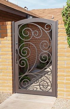 an iron gate is open on a brick wall and concrete walkway in front of a house