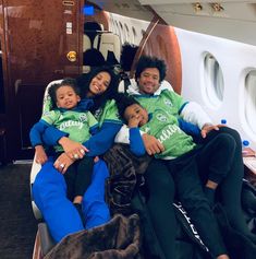 three people sitting on a bed in front of an airplane with their arms around each other