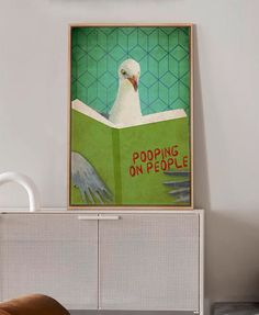 a white bird sitting on top of a green book next to a wall mounted clock