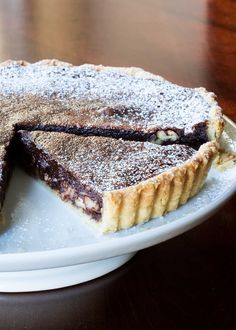 a chocolate pie on a white plate covered in powdered sugar sits on a wooden table