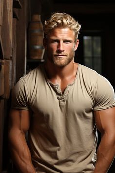 a man in a tan shirt leaning against a wooden wall with his hands on his hips