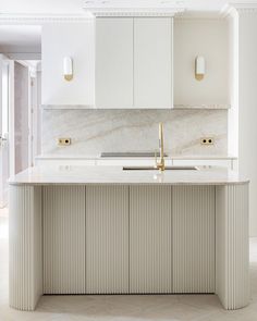 a white kitchen with marble counter tops and gold faucets on the sink area